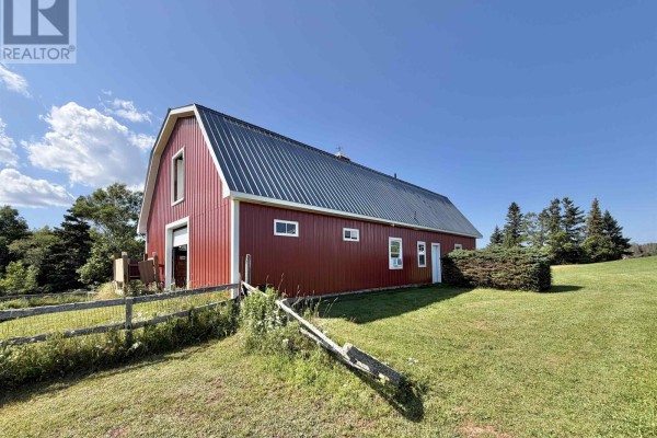 Red barn with white trim and a dark metal roof situated on a grassy field. - 8395 Rte 19, Bonshaw