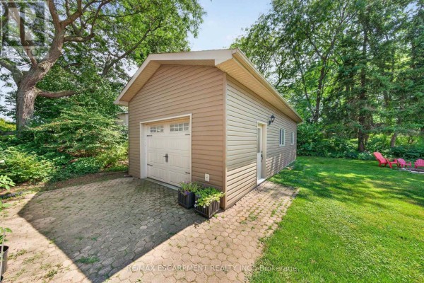 A detached garage with a white overhead door, beige siding, and a paver driveway. - 8399 Dickenson Road E, Hamilton