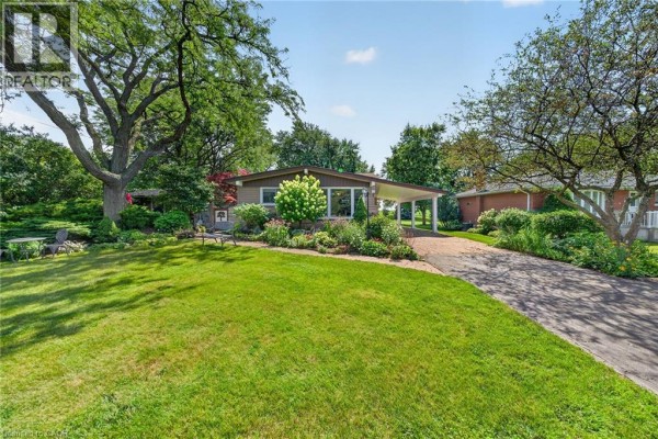 Exterior view of a beige bungalow with a driveway, carport, and lush green lawn. - 8399 Dickenson Road E, Mount Hope