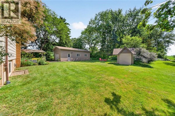 Rear yard view with a grassy lawn, detached garage, shed, and mature trees. - 8399 Dickenson Road E, Mount Hope