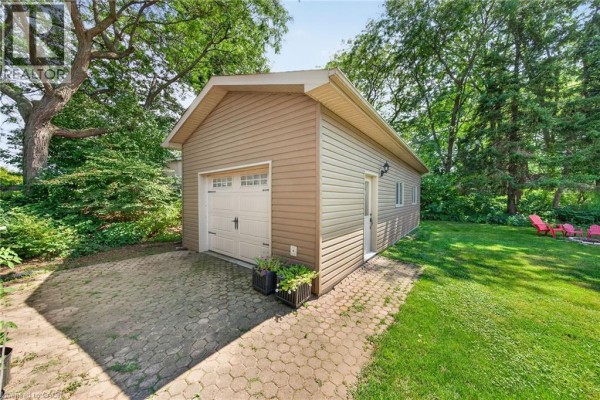 Detached garage with a double door, siding, and paver driveway in a green yard. - 8399 Dickenson Road E, Mount Hope
