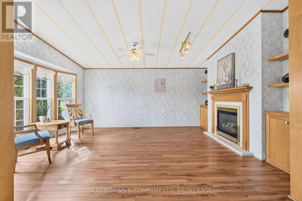 Spacious living room featuring wood flooring, a fireplace with wood cabinetry, and a large bay window with chairs. - 84 - 3033 Townline Road, Fort Erie