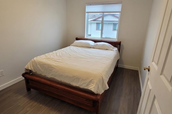 Bedroom with a wooden bed frame, white bedding, and a window overlooking the exterior. - 84 717 Aspen Rd, Comox