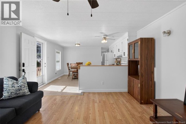 Open-concept living, dining, and kitchen area with white cabinets and wood-look flooring. - 84 Biddington, Moncton