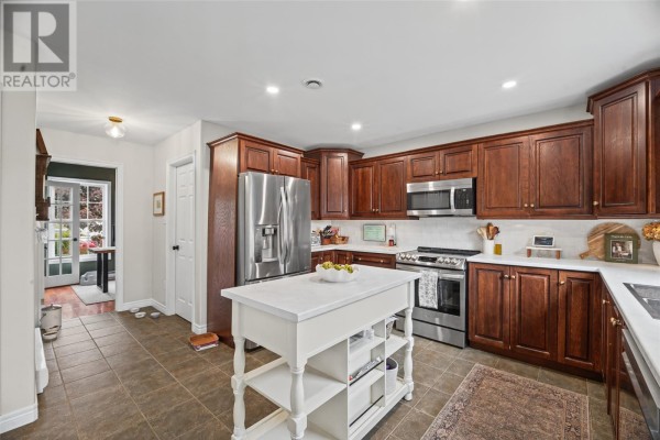 Kitchen with dark wood cabinets, stainless steel appliances, and a white island. - 84 Gil Eannes Drive, St  John S