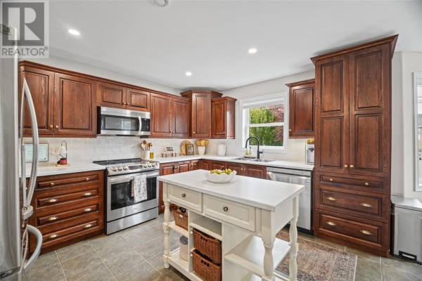 View of kitchen with dark wood cabinets, stainless steel appliances, and white island. - 84 Gil Eannes Drive, St  John S