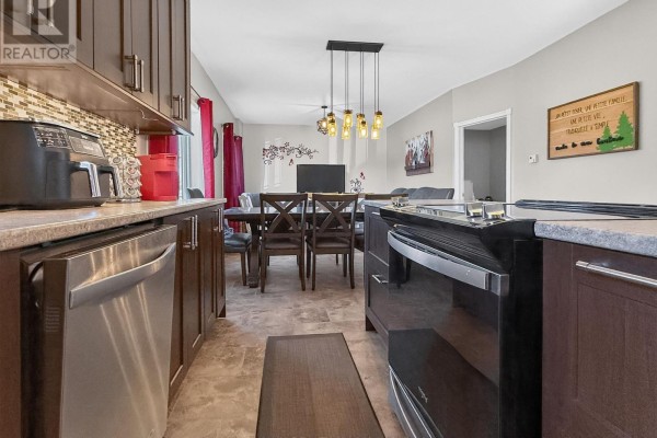 Kitchen and dining area with dark cabinets, stainless steel dishwasher, black range, and pendant lights.