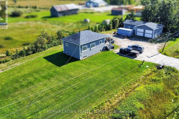 Side view of the grey house with a pitched roof, overlooking a vast expanse of green grass. - 84 Highway 11 Highway E, Hearst