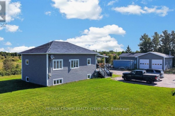 Exterior of the grey house showing the side entrance and a large detached garage with double doors. - 84 Highway 11 Highway E, Hearst