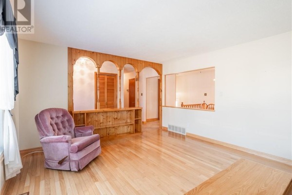 Living room with hardwood floors, plush armchair, and ornate wood archway. - 84 Neelon Avenue, Sudbury