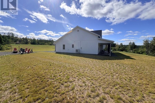Expansive green lawn surrounds a white house with a covered patio and a fire pit area. - 84 Road To The Isles Road, Lewisporte
