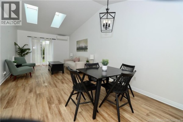 Living and dining area with vaulted ceiling, skylights, beige sofa, green chairs, and black dining set. - 84 Seaman Street Unit# 5, Moncton