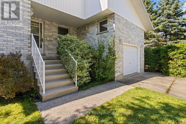 Front entrance stairs and side view of the garage door of a grey brick house. - 840 Mcnaughton Street, South Bruce Peninsula