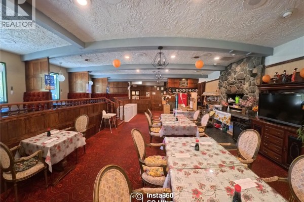 Restaurant dining area with red carpet, wooden booths, tables, and stone fireplace. - 8405 Byng Rd, Port Hardy