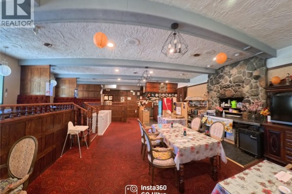 Restaurant dining room with tables, wooden dividers, stone fireplace, and beverage station. - 8405 Byng Rd, Port Hardy