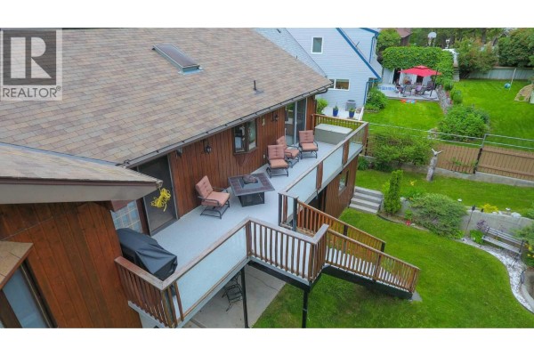 Deck with outdoor furniture and a gas grill overlooks a green backyard with mature trees. - 8408 Richardson Crescent, Canal Flats