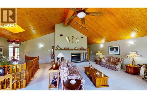 Living room with sofas, fireplace, wood-paneled vaulted ceiling, and decorative wall items. - 8408 Richardson Crescent, Canal Flats