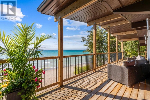 Wooden deck with a glass-top table and chairs, featuring a stone outdoor fireplace. - 84153 Lakeland Estates Road, Ashfield Colborne Wawanosh
