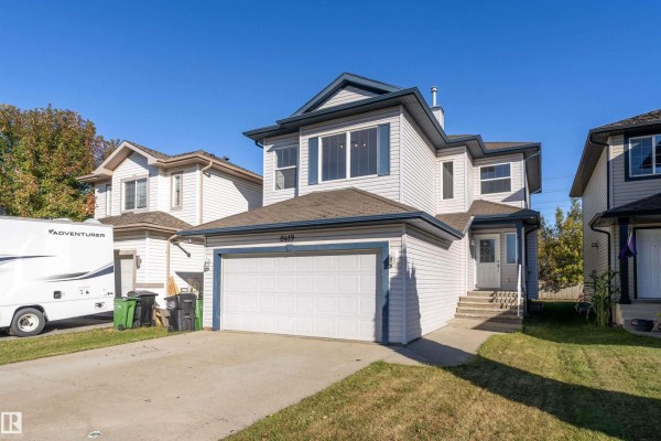 Front exterior view of a light blue two-story house with a double garage door and a dark blue roof. - 8419 2 Av Sw, Edmonton