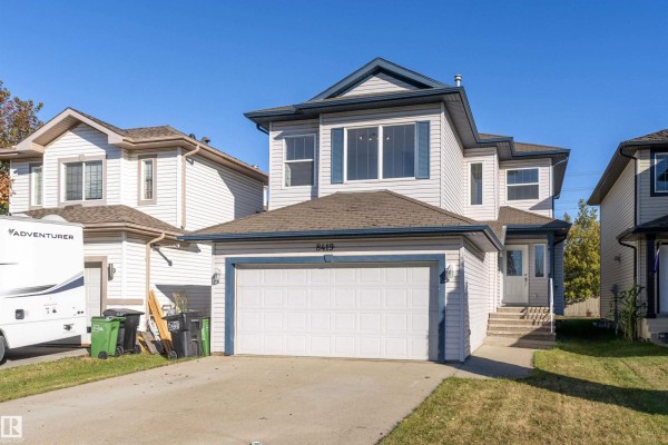 Front exterior view of a light blue two-story house with a double garage door and a dark blue roof. - 8419 2 Av Sw, Edmonton