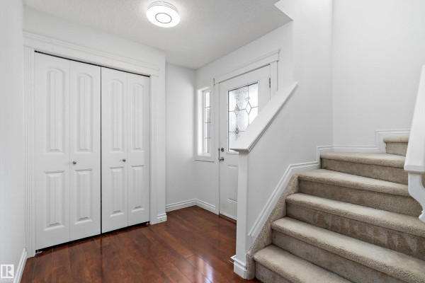 Interior view of a home entrance with a white door, a large closet, and a carpeted staircase. - 8419 2 Av Sw, Edmonton