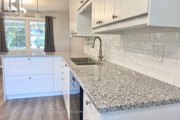 Detailed view of the kitchen counter with a sink, faucet, backsplash, and white cabinets. - 843 Driftwood Road, London North