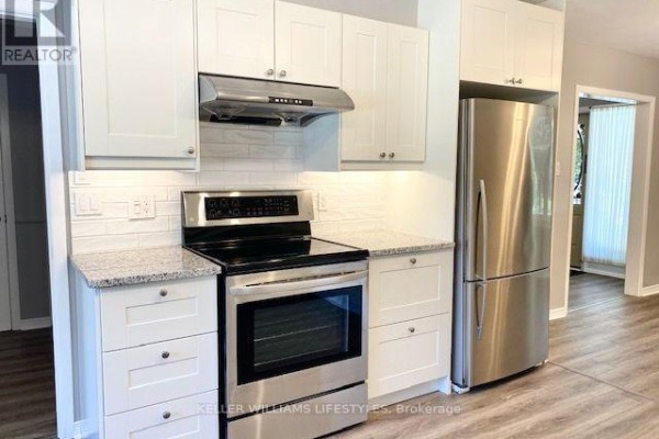 Kitchen area featuring a stainless steel stove, refrigerator, white cabinets, and a view into an adjacent room. - 843 Driftwood Road, London North