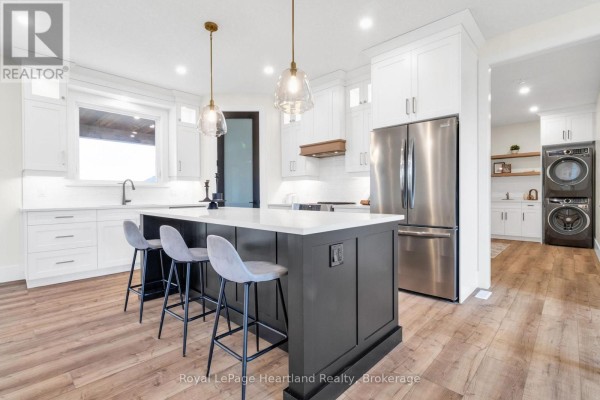 Modern kitchen with an island, white cabinetry, stainless steel appliances, and pendant lighting. - 84347 Kent Line, Huron East