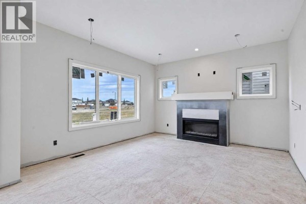 Unfinished living room with grey walls, large windows, and a fireplace with a dark grey surround. - 844 Hampshire Crescent Ne, High River
