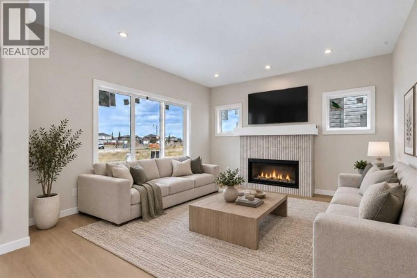Staged living room with light beige sofas, a coffee table, and a fireplace with a white tiled surround. - 844 Hampshire Crescent Ne, High River