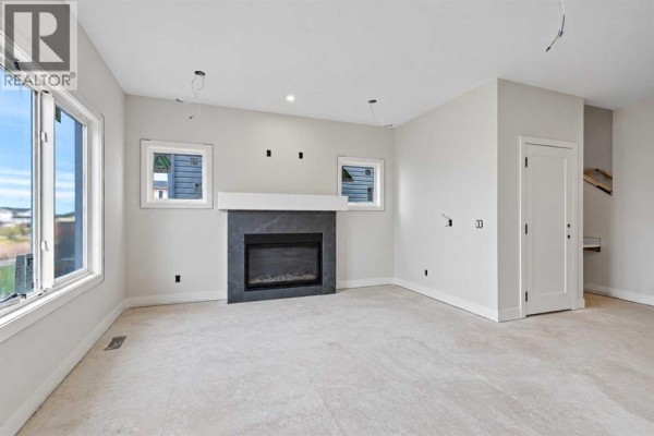 Living room showing a white door, unfinished grey walls, and a modern fireplace with dark grey surround. - 844 Hampshire Crescent Ne, High River