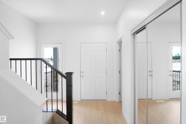 Interior hallway featuring white doors, blonde wood floors, and mirrored closet doors. - 8444 183 Av Nw, Edmonton