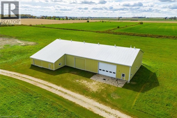 Exterior of a long, yellow workshop with a white metal roof and a large roll-up door. - 8449 Line 2, Arthur