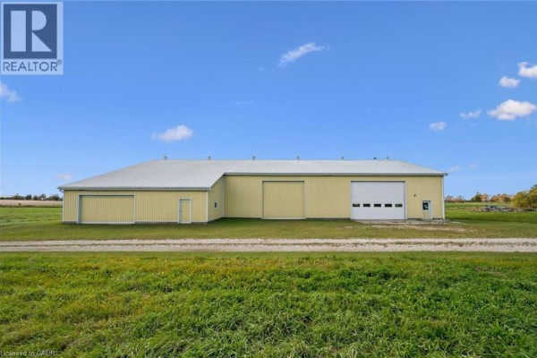 Side view of a yellow workshop with a white metal roof and multiple large garage doors. - 8449 Line 2, Arthur