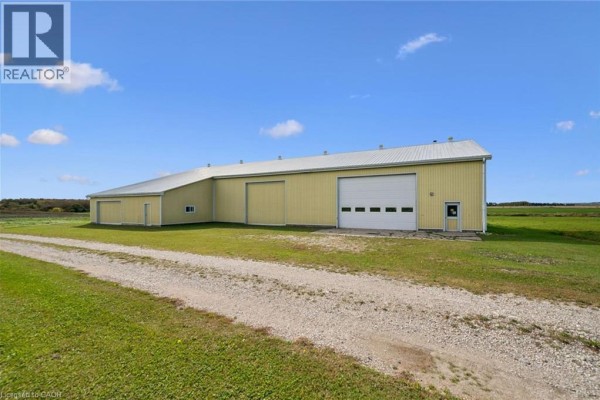 Gravel driveway leading to a yellow workshop with a white metal roof and a large roll-up door. - 8449 Line 2, Arthur
