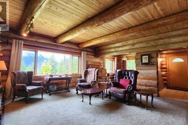 Living room with log walls, exposed beams, large picture window, and plush seating. - 8470 Red Mountain Road, Silverton