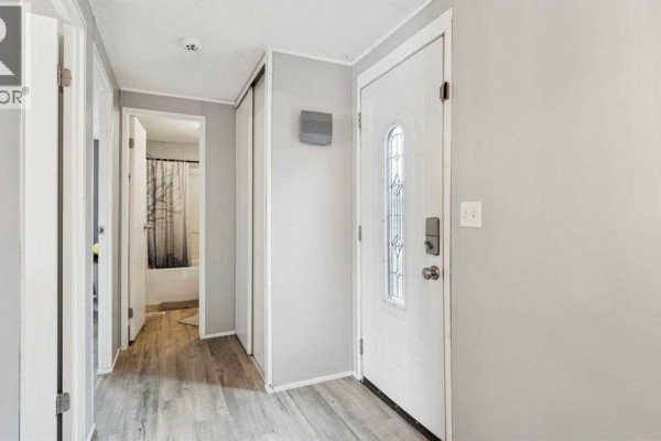 Interior hallway with a white front door and a doorway leading to a bathroom. - 848 Madison Drive, Irricana