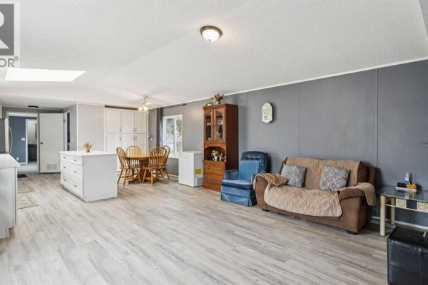Living area with a brown sofa, blue armchair, wooden china cabinet, and dining set. - 848 Madison Drive, Irricana