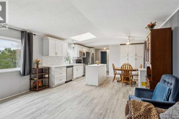 Open concept living, dining, and kitchen area with light gray walls and wood flooring. - 848 Madison Drive, Irricana