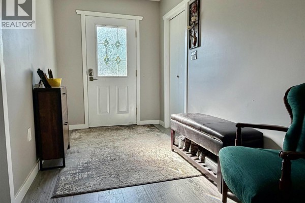 Interior entrance hallway with a grey rug, dark wood cabinet, and a green armchair. - 8490 Louise Drive, Prince George