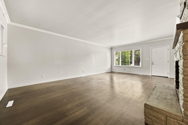 Empty living room with light grey walls, dark hardwood floors, and a stone fireplace. - 8495 164 Street, Surrey
