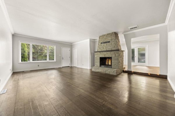 Living room with dark hardwood floors, stone fireplace, and views into an adjacent room. - 8495 164 Street, Surrey