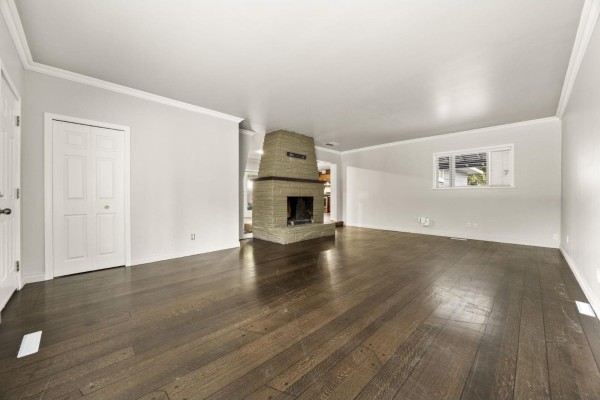 Spacious living area with dark hardwood floors, a stone fireplace, and a closet door. - 8495 164 Street, Surrey