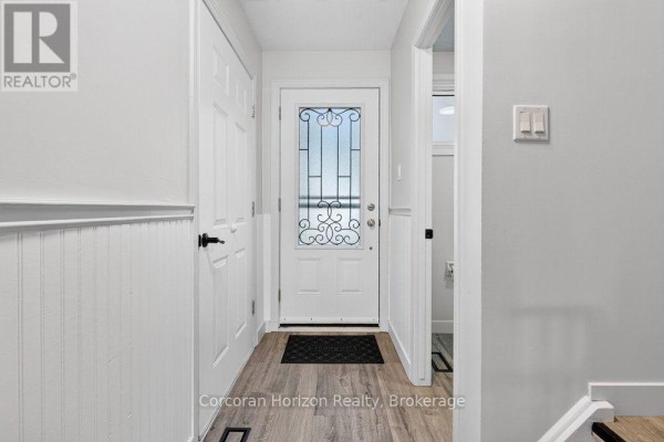 Interior view of the foyer with a white door, wainscoting, and wood-look flooring. - 85 - 100 Quigley Road, Hamilton