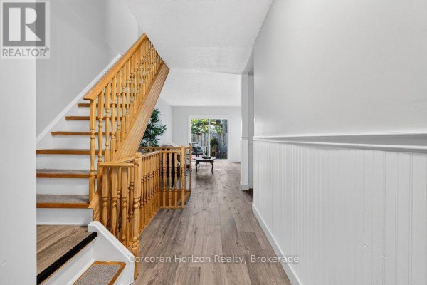 Hallway inside townhouse showing a wooden staircase with carpeted treads and access to the living area. - 85 - 100 Quigley Road, Hamilton