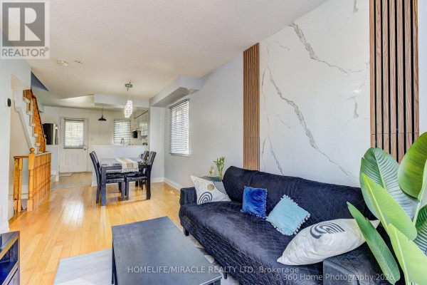 Living room with a black sofa, marble accent wall, dining area, and hardwood floors. - 85 - 2 Hedge End Road, Toronto