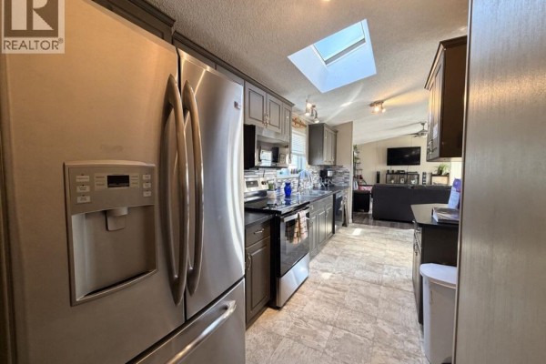 Kitchen area with stainless steel refrigerator and dark cabinets, with a view towards the living room. - #85 9824 104 Avenue, Clairmont