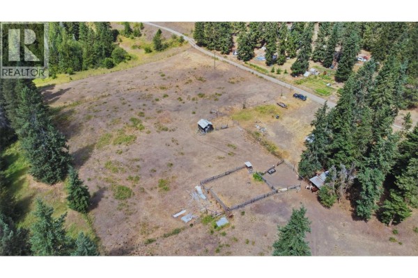 Aerial view of the property showing the mobile home, a large field, and wooded area. - 85 Candide Drive, Lumby