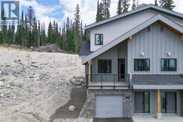 Close-up of duplex entrance with stone base, deck, and mountain backdrop. - 85 Creekside Trail, Big White