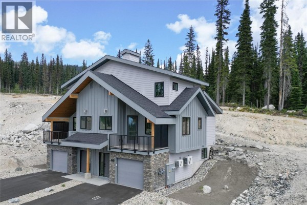 Side view of duplex with garages, balconies, and dense forest behind. - 85 Creekside Trail, Big White